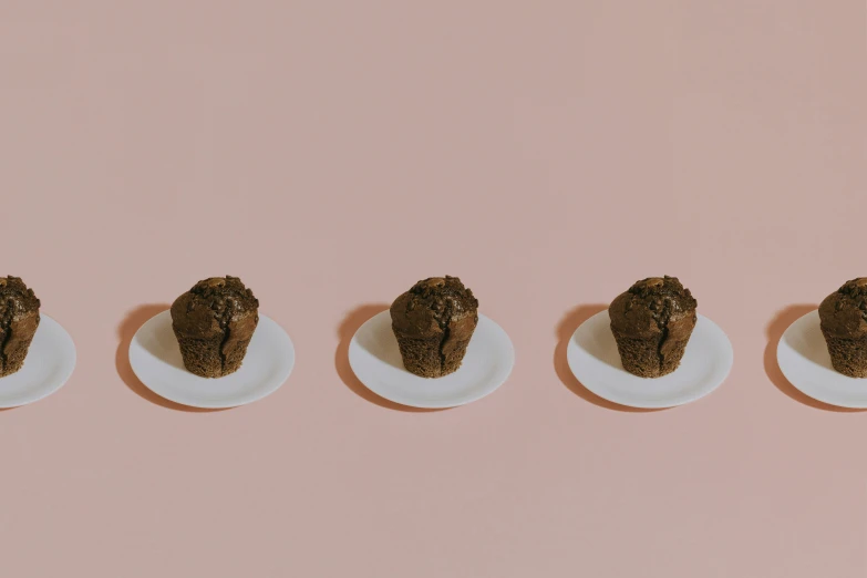 a line of desserts are on plates sitting on a pink surface