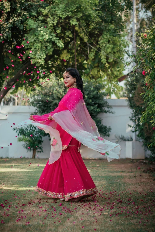 a woman in pink wearing a red sari and carrying soing with pink flowers on it