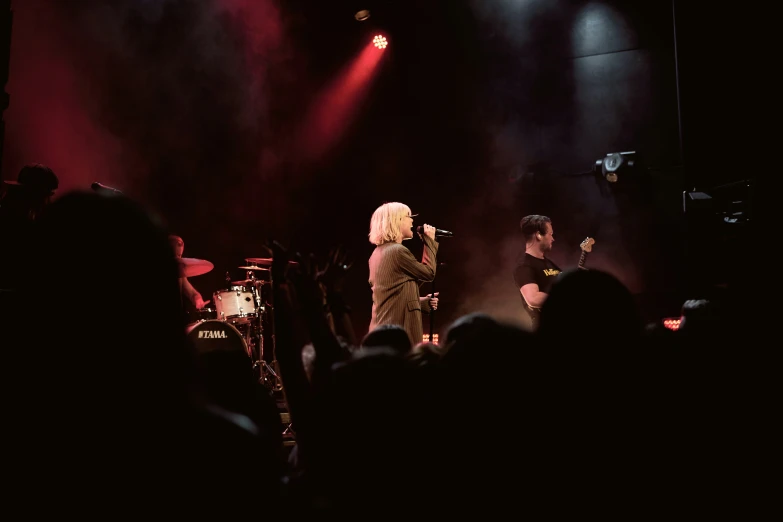 a man is singing into a microphone as other people watch from behind