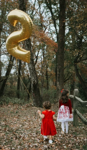 two children holding gold balloon shaped like the letter s