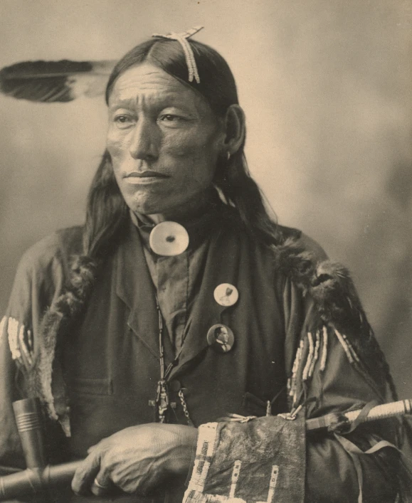a native indian holds a stick and looks up