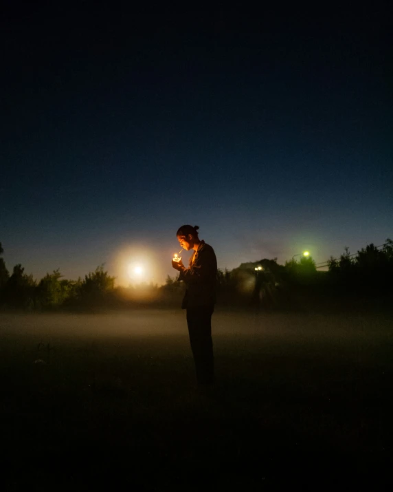 the person standing outside holds his cell phone up to his ear as lights shine on