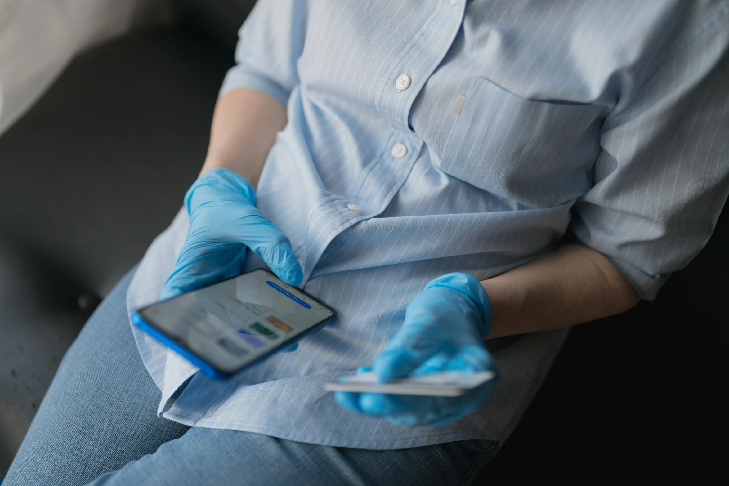 a person sitting on the sofa, holding an electronic device and protective gloves