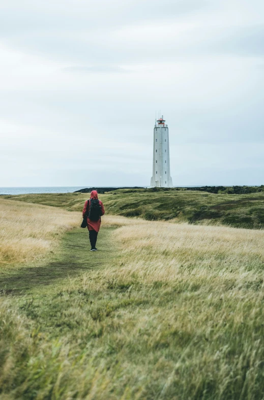 a person walking in the grass towards a light house