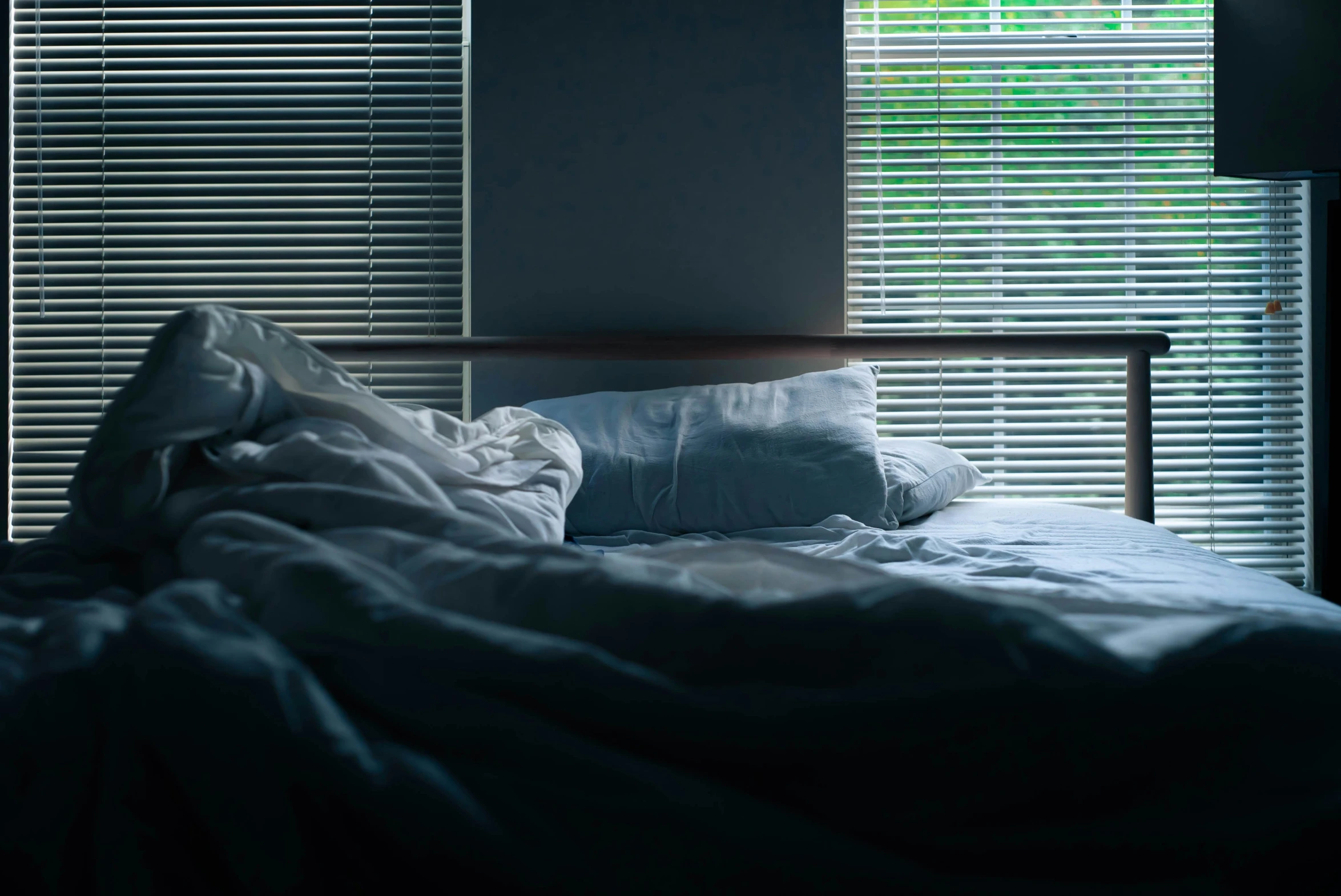 an unmade bed is in front of window with the covers pulled back