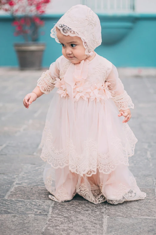 baby girl in an old fashioned dress and bonnet in a courtyard