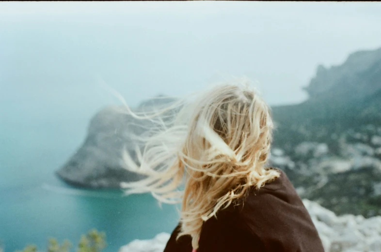 the blonde haired woman with her hair blowing in wind looking out over the sea