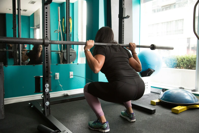 a woman squats as she lifts up a bar in the gym