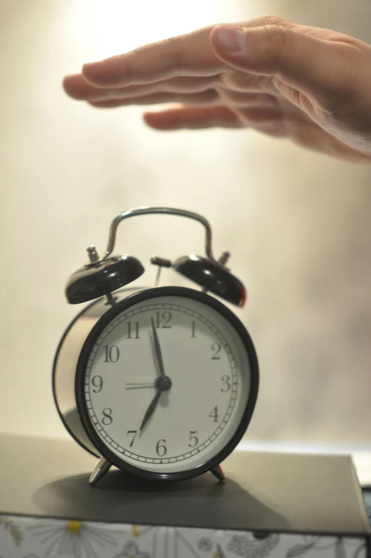 a hand reaching out towards a clock on top of a cube