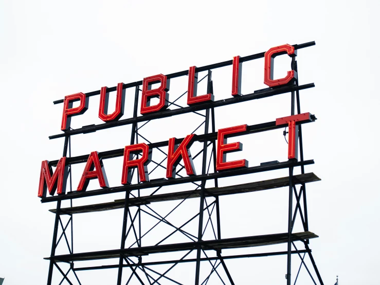 a large red public market sign sitting on top of a tall metal structure