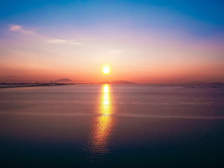 the sun rising over the ocean with water and buildings