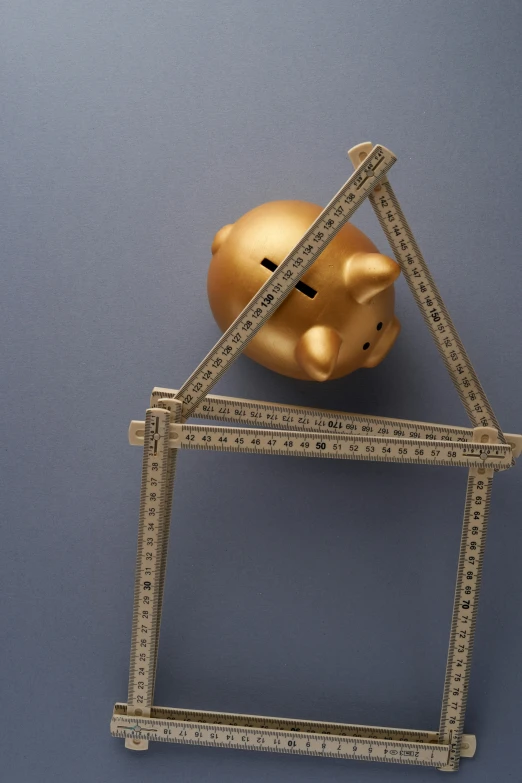 a small golden piggy bank is stacked on top of a pair of rulers