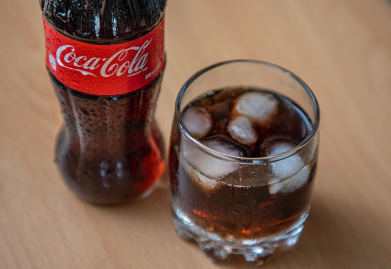 two bottles filled with coke next to a glass full of ice