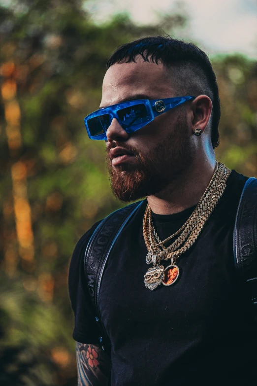 a man wearing sunglasses and necklace standing by a forest