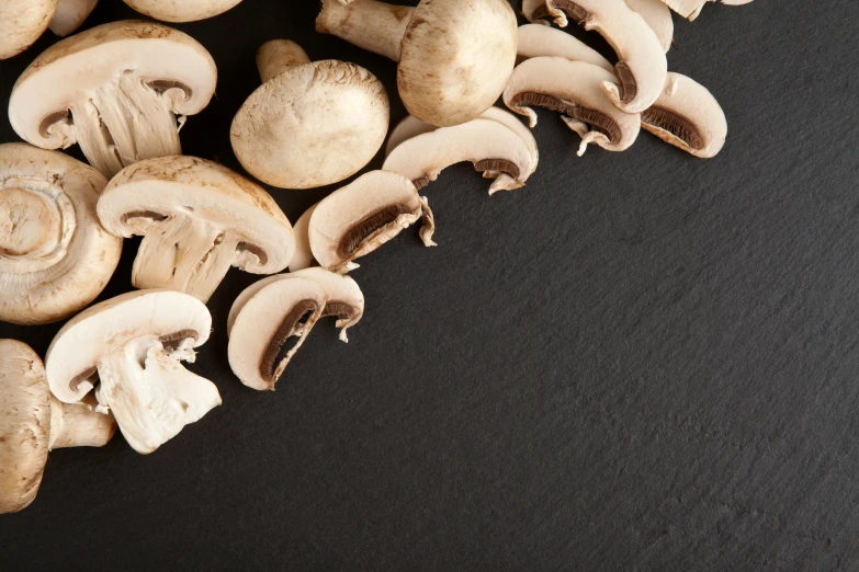 several cut mushrooms sit in the middle of black surface