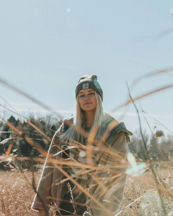 a beautiful young woman standing in a wheat field wearing a hat