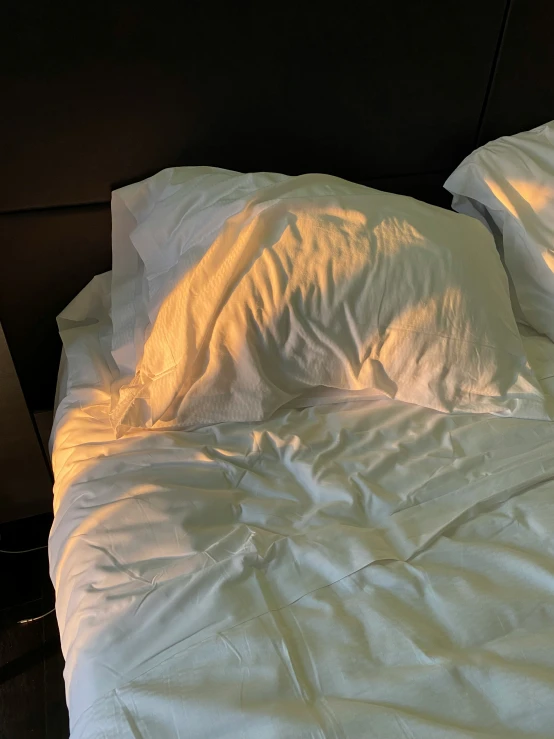 the light shines on two unmade bedsheets