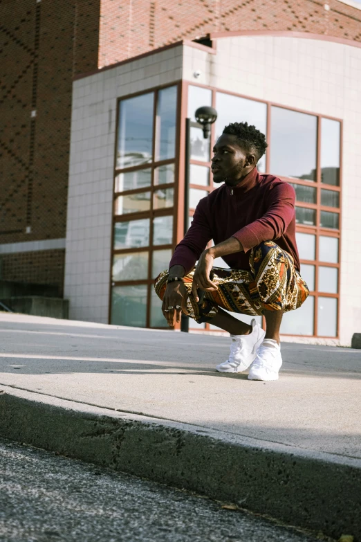 a man in a red sweater kneeling on concrete in front of a building