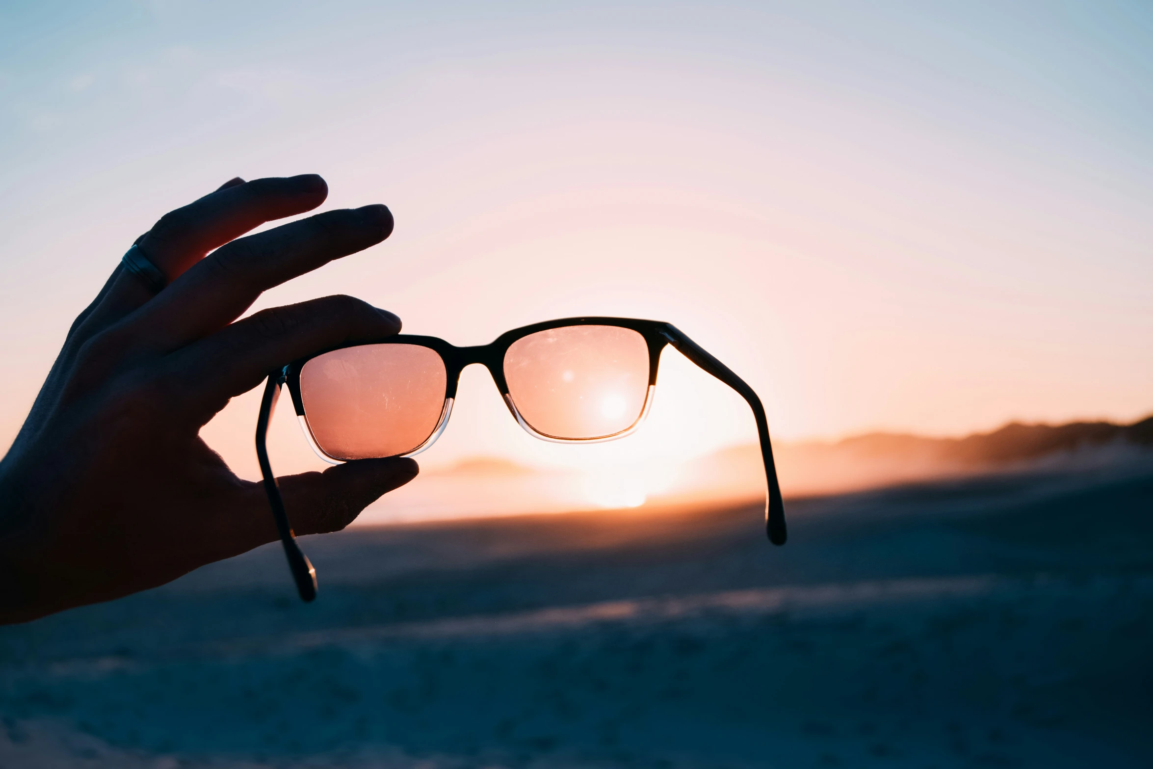 a person's hand holding up two glasses in the sunset