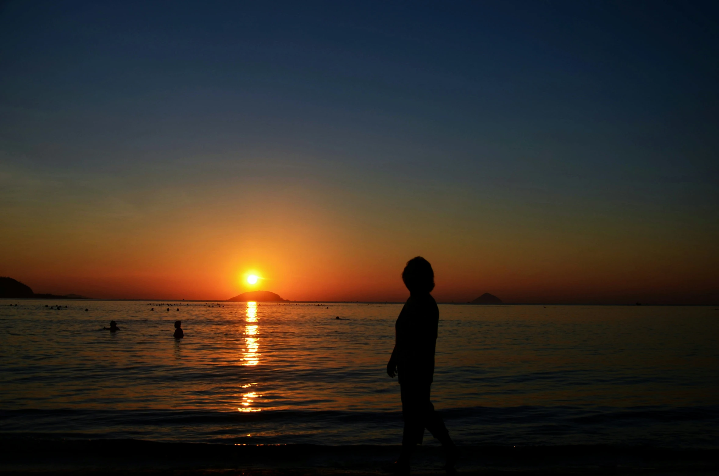 man looking out to sea at sunset over calm ocean