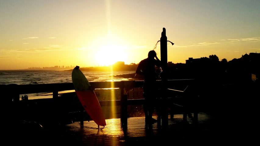 a person is standing at the end of a pier holding a surfboard at sunset