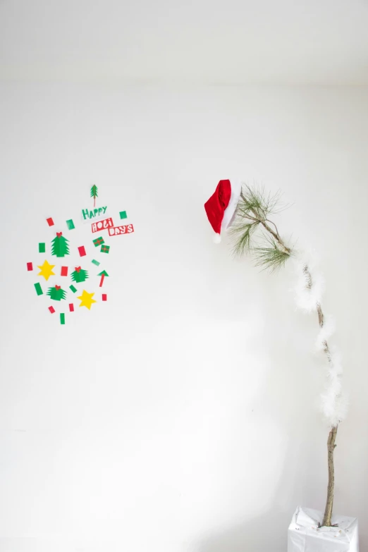 a decorated tree with santa hat next to a white wall