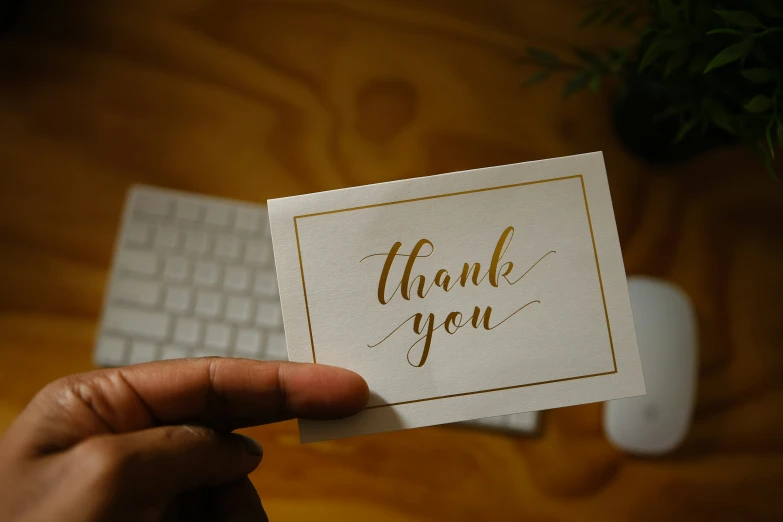 a hand holding up a small card with a thank message written on it