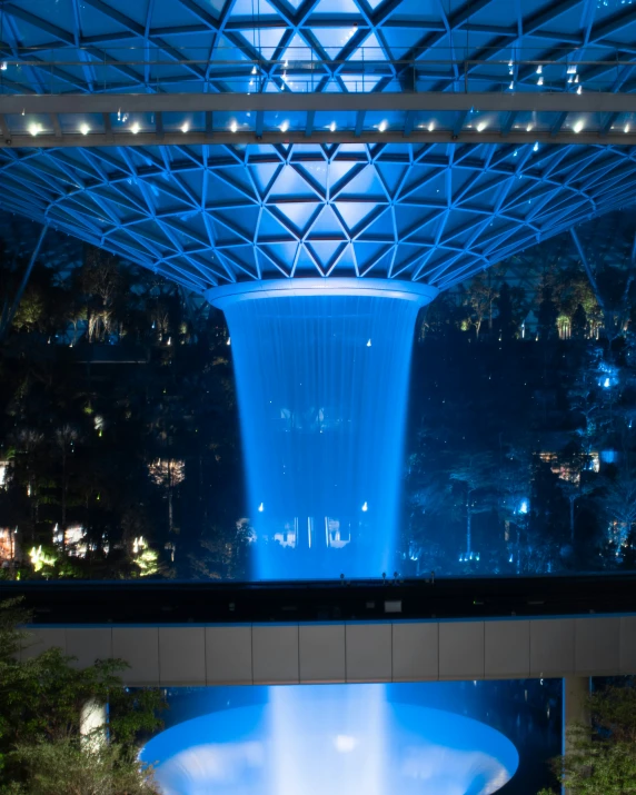 blue lit waterfall in indoor atrium with trees on cliff