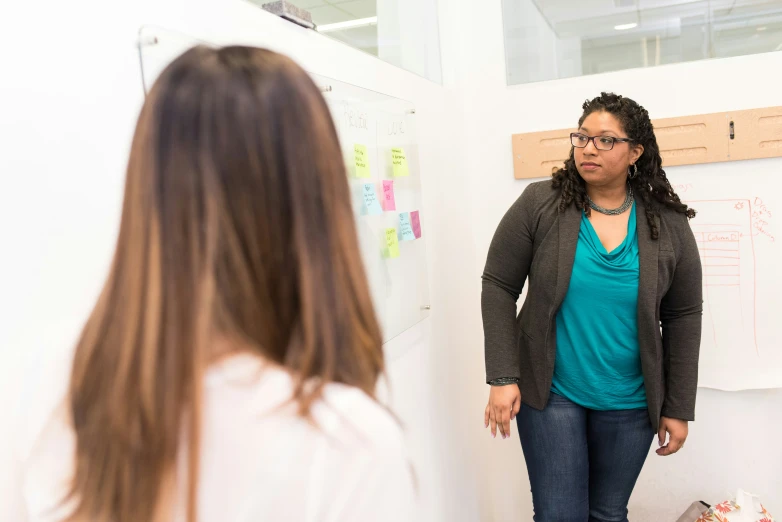 two women are having a discussion in front of a white board