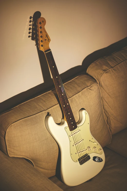 a white electric guitar is resting on the couch