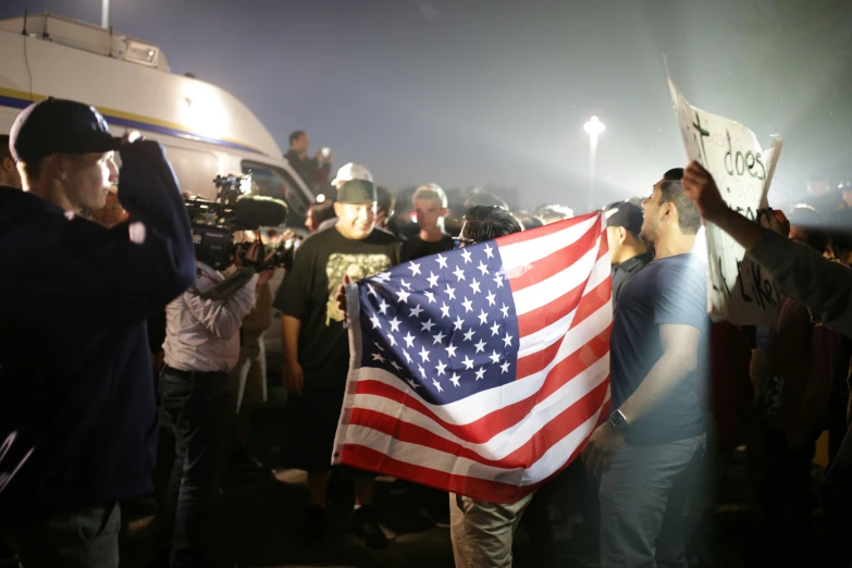 a crowd standing around a large american flag