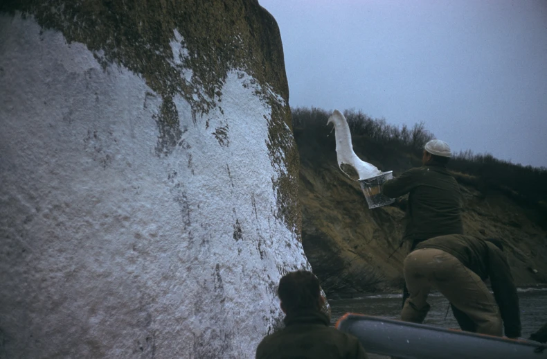 two men holding their canoes on a boat near a cliff