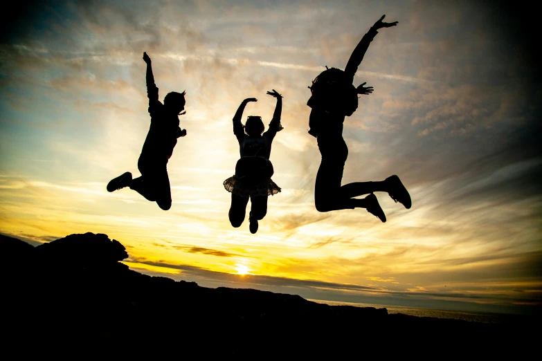three people jumping into the air on top of a beach