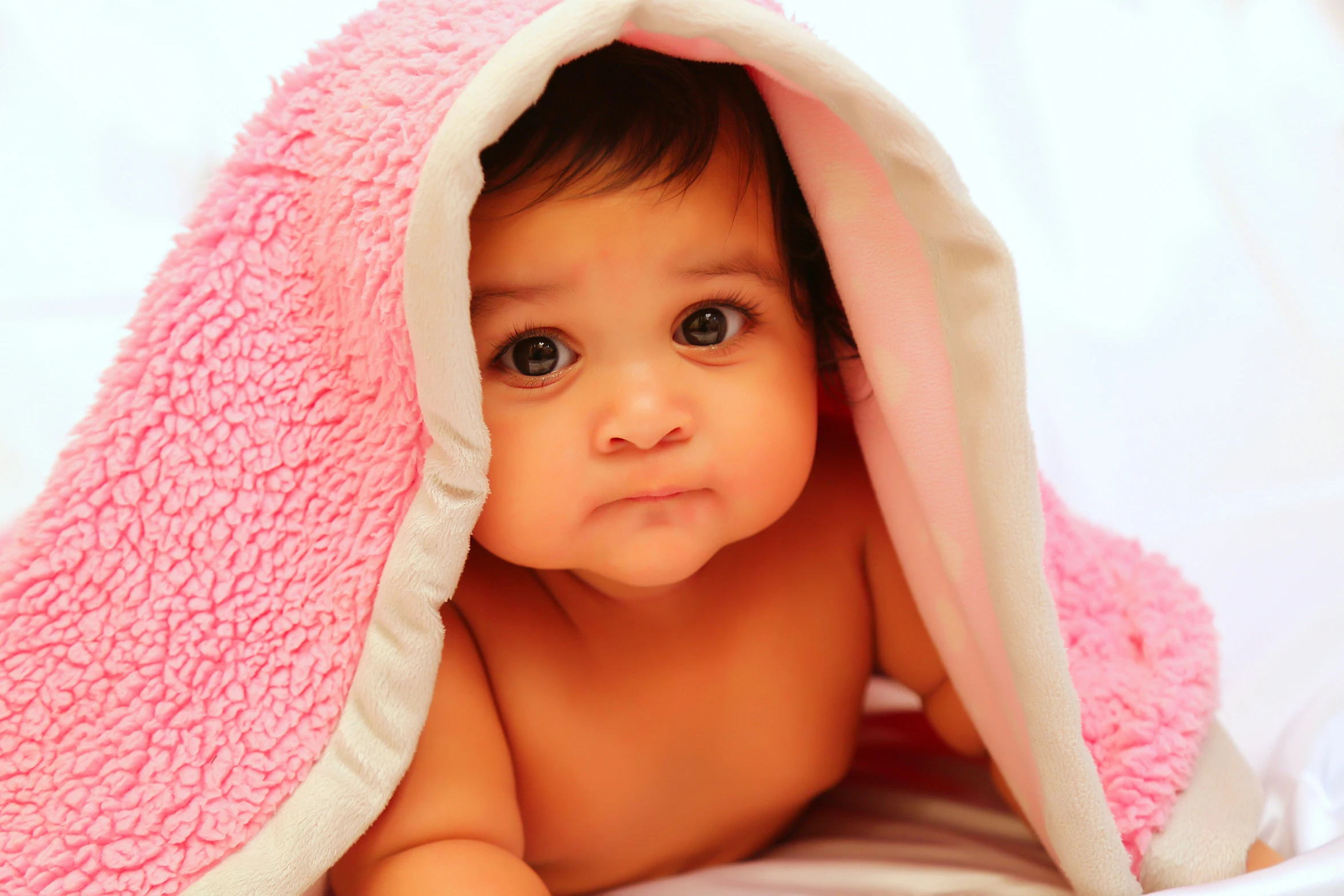 a baby with brown eyes under a pink blanket