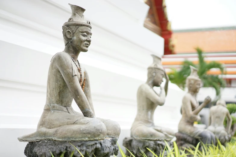 three statues sitting in the grass with a person praying