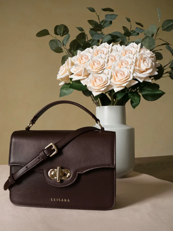 white roses sitting beside a purse, next to a vase with roses