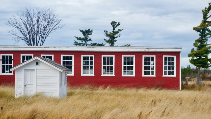 an old red building with white windows stands in tall dry grass