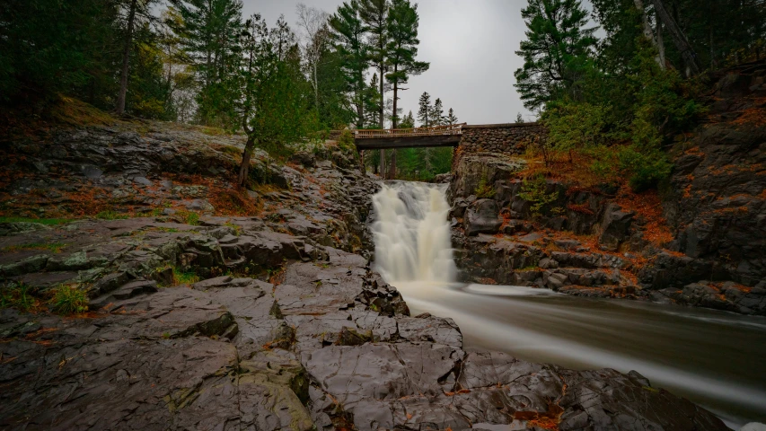 a waterfall flowing under a bridge near some rocks