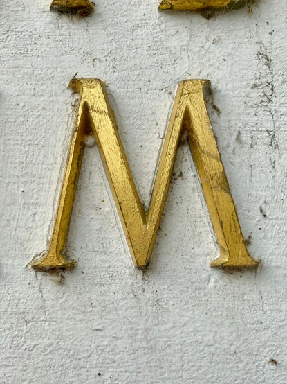 a gold letter m is on a white wall