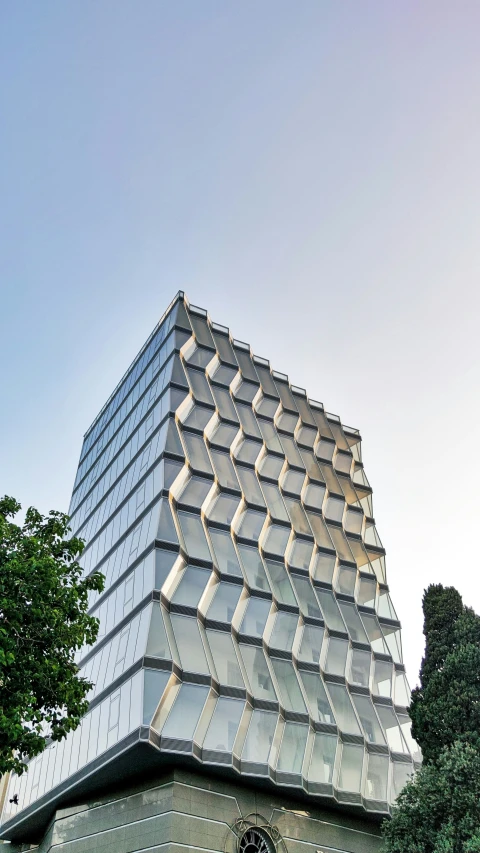 the large building with an unusual roof stands in front of trees