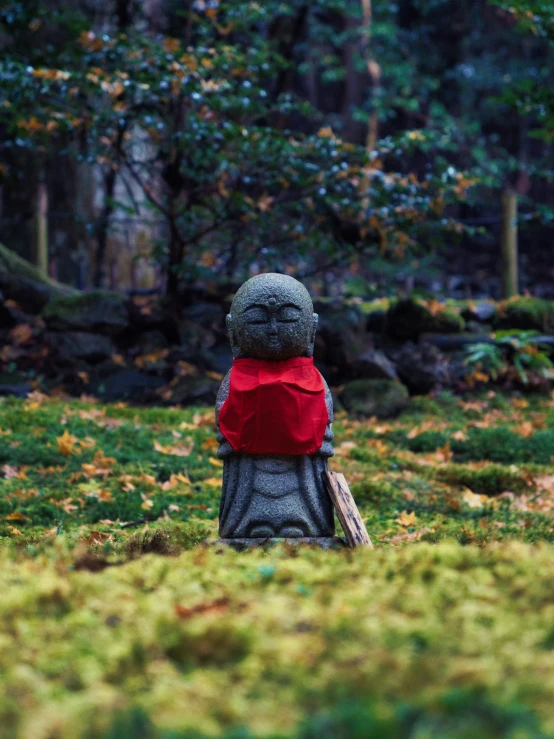 a statue sitting in the grass surrounded by forest