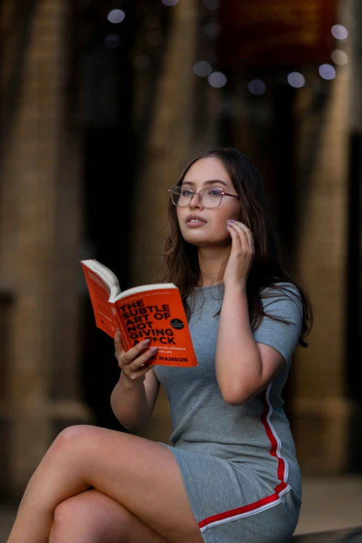 woman in gray dress sitting reading an orange book