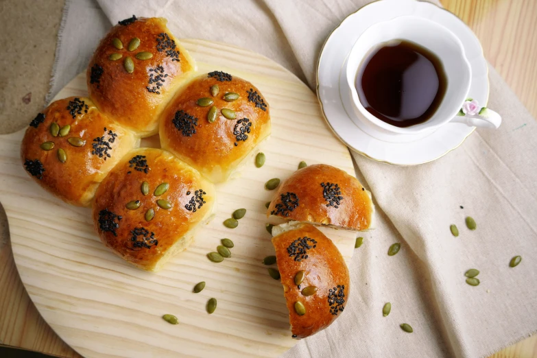 some small rolls with seeds are on a board near a cup of tea