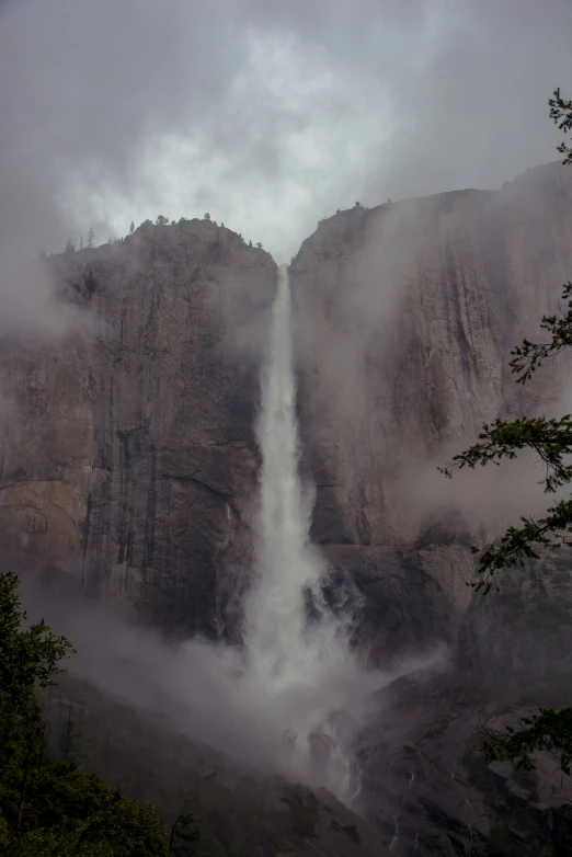 a waterfall rises into a dark foggy mountain