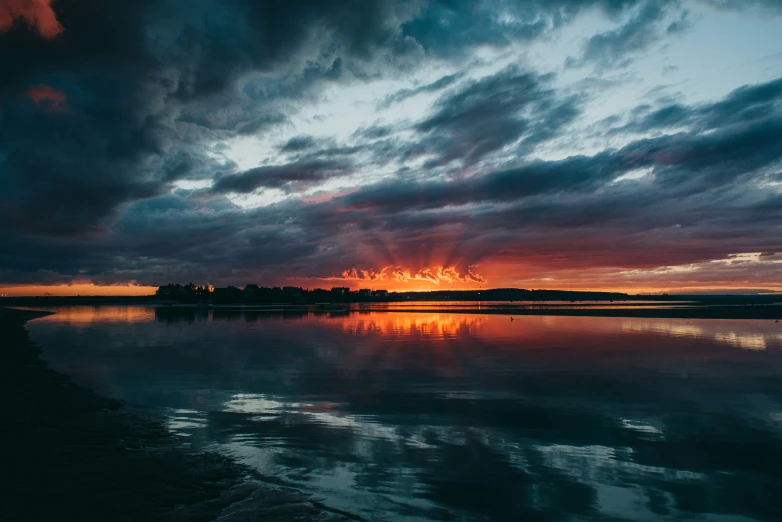 an orange sunset with clouds reflecting in water