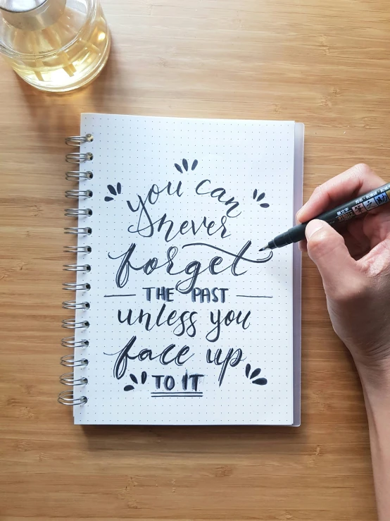 a woman's hand holding a black marker while writing a note on a notebook