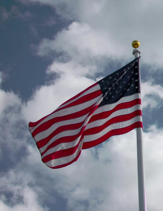 an american flag on a pole in front of a blue cloudy sky