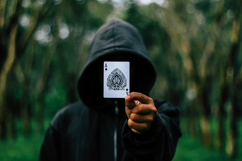 a hooded person holding up a card in their hand