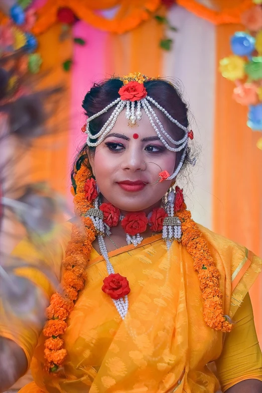 a woman in orange and yellow sari standing near flower garlands