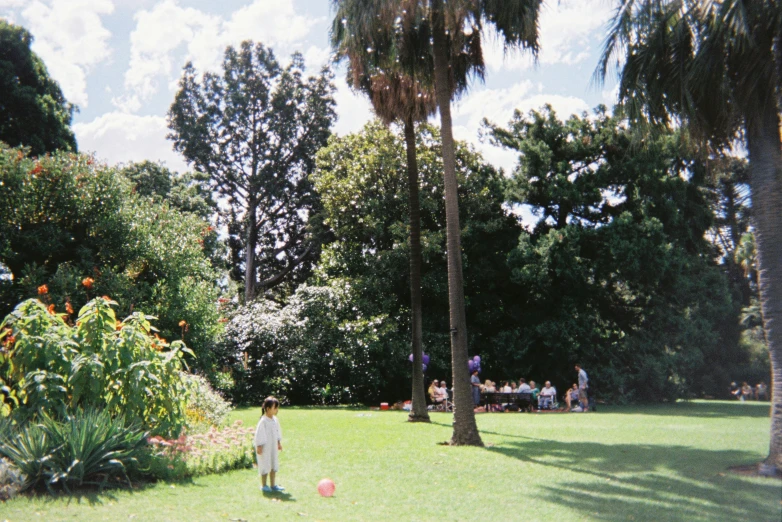 a child in a white jacket playing with a pink ball in a lush green garden